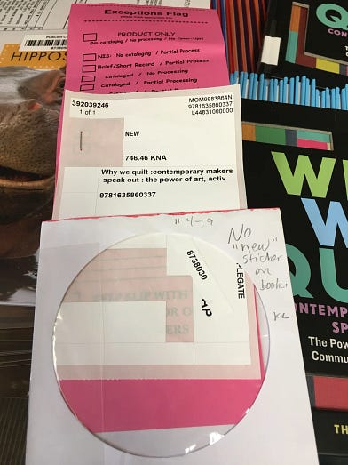 A pink Baker & Taylor product-only exception slip placed on top of library books and paperwork, with handwritten notes and a date.